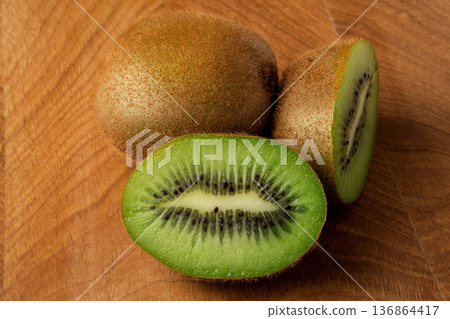 Kiwi one whole and one cut in half lie on a wooden board Kiwi one whole and one cut in half lie on a wooden board 136864417