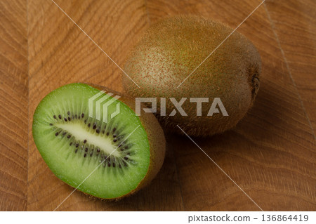 Kiwi one whole and cut off part lie on a wooden board Kiwi one whole and cut off part lie on a wooden board 136864419