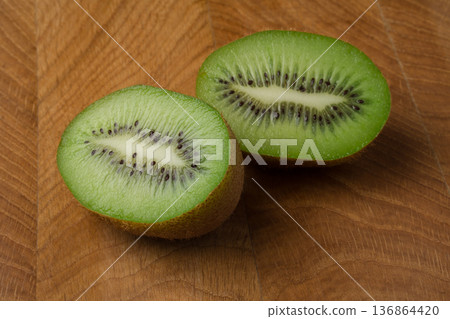 Kiwi cut in two equal shares, lies on a wooden board Kiwi cut in two equal shares, lies on a wooden board 136864420