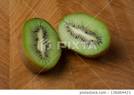 Kiwi cut in two equal shares, lies on a wooden board 136864421