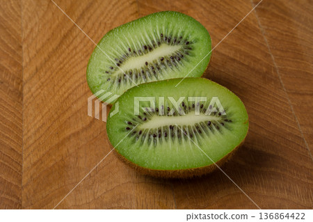 Kiwi cut in two equal shares, lies on a wooden board Kiwi cut in two equal shares, lies on a wooden board 136864422