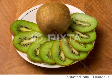 Kiwi single whole and sliced in pieces in a white plate and on a wooden board 136864424