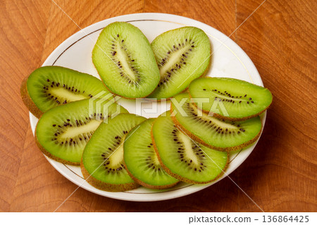 Kiwi single whole and sliced in pieces in a white plate and on a wooden board Kiwi single whole and sliced in pieces in a white plate and on a wooden board 136864425