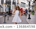 Woman in white dress walking on luxury holiday shopping street 136864598