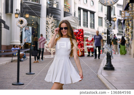 Woman in white dress walking on luxury holiday shopping street Woman in white dress walking on luxury holiday shopping street 136864598