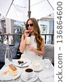 Young woman in sunglasses enjoying coffee and dessert at outdoor cafe 136864600