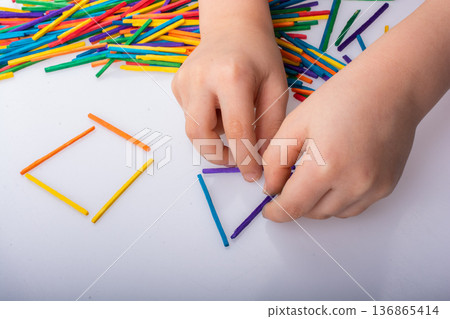 Kid making geometric shapes with colorful sticks on white background Kid making geometric shapes with colorful sticks on white background 136865414