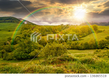 sunset over rural area in the valley. green countryside scenery with wooded rolling hills. mountain landscape in springtime. remote place for weather photography under rainbow 136865519