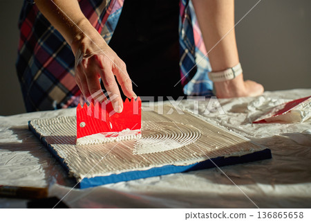 Hand pressing red plastic scraper into thick paste to form curved textured lines Hand pressing red plastic scraper into thick paste to form curved textured lines 136865658
