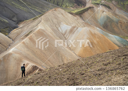 Hiker on a ridge looking on colorful mountains and ridges in front of him, Highlands, Iceland 136865762