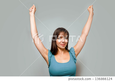 Woman with arms raised smiling in a neutral room during the daytime celebrating a personal success or achievement 136866124