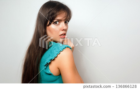 Woman looks back with surprise in a simple setting, expressing a sense of intrigue, while casually dressed with long hair and a neutral background Woman looks back with surprise in a simple setting, expressing a sense of intrigue, while casually dressed with long hair and a neutral background 136866128