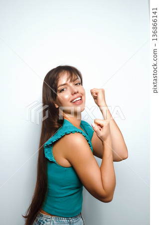Woman flexes her muscles and smiles with confidence in a studio setting during the day 136866141