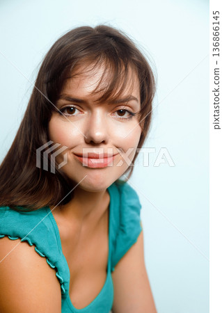 Smiling woman with dark hair wearing a blue top posing against a light background in a studio setting during daytime 136866145