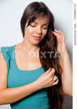 Woman with long hair plays with her hair while smiling indoors in a simple setting during daytime 136866147