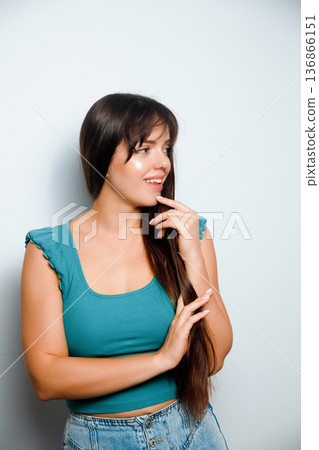Woman smiles and looks to the side while posing in a studio setting with a plain background Woman smiles and looks to the side while posing in a studio setting with a plain background 136866151