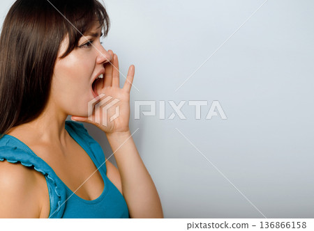 Woman shouts or calls out with enthusiasm in a simple indoor setting during the day Woman shouts or calls out with enthusiasm in a simple indoor setting during the day 136866158
