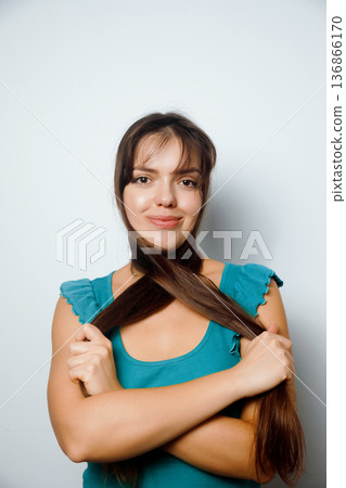 Woman poses with long hair styled in a unique way while wearing a blue top in a simple indoor setting Woman poses with long hair styled in a unique way while wearing a blue top in a simple indoor setting 136866170