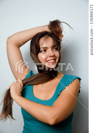 Woman playfully styling her long hair in a creative way in a simple indoor setting during the daytime Woman playfully styling her long hair in a creative way in a simple indoor setting during the daytime 136866171