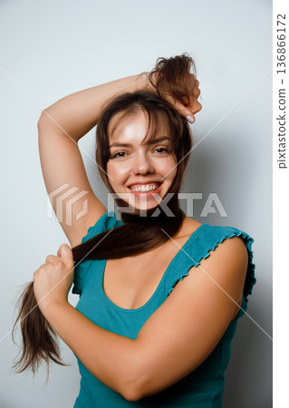 Woman playing with long hair while smiling against a plain background during daytime Woman playing with long hair while smiling against a plain background during daytime 136866172