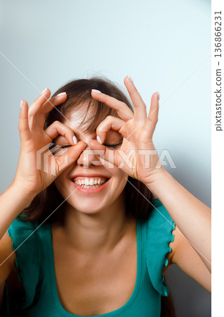 Young woman makes funny face while holding her fingers to her eyes in a playful act during daytime gathering Young woman makes funny face while holding her fingers to her eyes in a playful act during daytime gathering 136866231