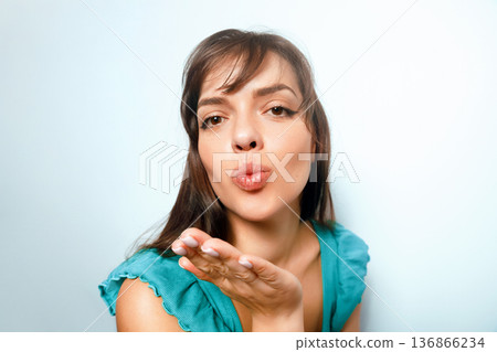 Woman blowing a kiss with a light blue background while wearing a blue top, showcasing a cheerful expression 136866234