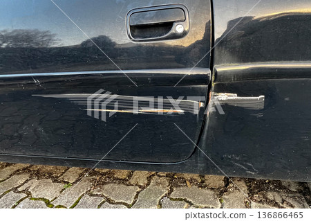 Scratched black car door with visible paint damage and rust marks close up of vehicle body after minor accident outdoors. 136866465