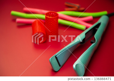 Side view of a green hair straightener with a twisted ceramic canvas on a background of curlers of different shapes and sizes on a pink background. The concept of styling, hairstyle, curls. High 136866471