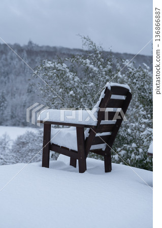 Single wooden chair standing in deep fresh snow against open winter landscape. Minimal composition emphasizing solitude, silence and vast natural space under cloudy sky. Single wooden chair standing in deep fresh snow against open winter landscape. Minimal composition emphasizing solitude, silence and vast natural space under cloudy sky. 136866887