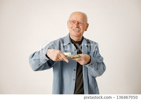 Senior gentleman with money on a white background. Man wearing blue t-shirt. Man waste money thowing it. Senior gentleman with money on a white background. Man wearing blue t-shirt. Man waste money thowing it. 136867050