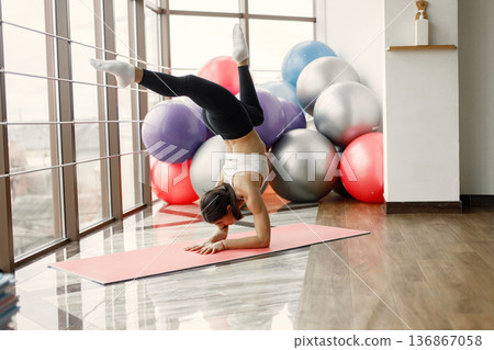 Fitness girl working out at gym with big window. Girl wearing black leggins and sport top. Young woman standing on hands. 136867058