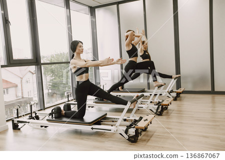 Three young fit women training in gym. Women wearing black sportwears. Caucasian girls excercising with equipment. 136867067