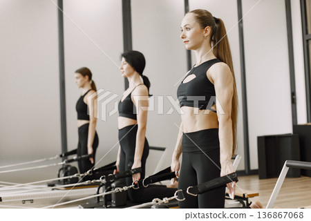 Three young fit women training in gym. Women wearing black sportwears. Caucasian girls excercising with equipment. Three young fit women training in gym. Women wearing black sportwears. Caucasian girls excercising with equipment. 136867068