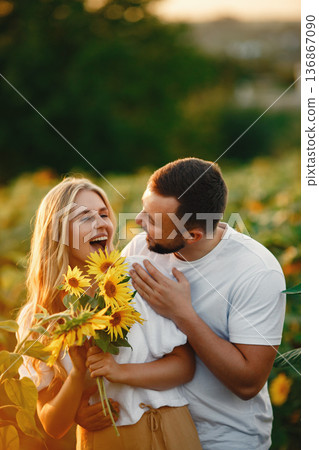 Young loving couple is kissing in a sunflower field. Portrait of couple posing in summer in field. Young loving couple is kissing in a sunflower field. Portrait of couple posing in summer in field. 136867090