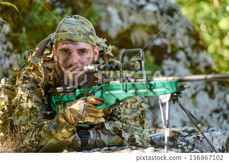 Camouflaged Sniper Soldier Lying in Woods With Precision Rifle and Scope During Field Operation 136867102