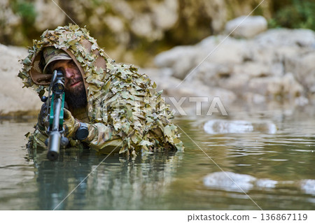 Camouflaged Sniper Soldier Lying in Shallow River With Rifle and Scope During Reconnaissance Camouflaged Sniper Soldier Lying in Shallow River With Rifle and Scope During Reconnaissance 136867119