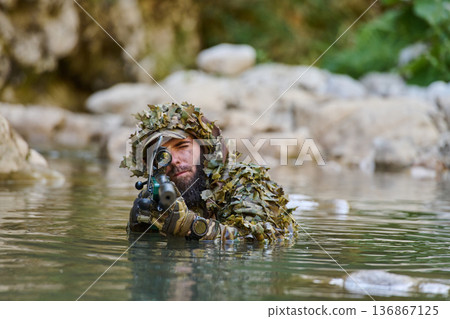 Camouflaged Sniper in Ghillie Suit Wading Through Water Aiming Rifle Through Scope 136867125