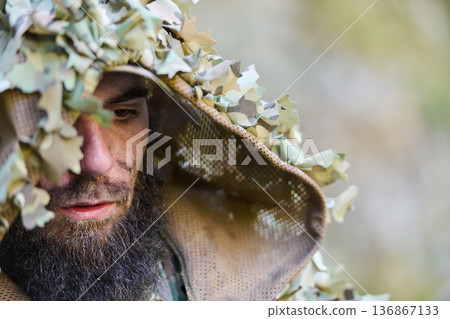 Camouflaged Soldier In Ghillie Hood Close-Up Portrait Of Tactical Sniper In Woodland Concealment 136867133