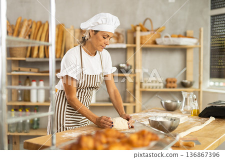 Elderly woman kneads dough in bakery Elderly woman kneads dough in bakery 136867396