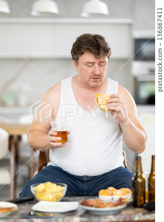 man drinks beer and eats a burger man drinks beer and eats a burger 136867411