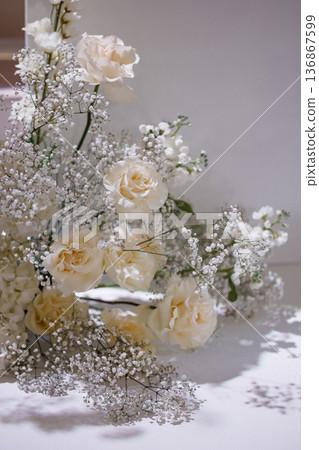 Cream roses and baby's breath arrangement with frosted branches on white table 136867599