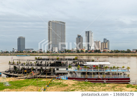 River cruise boats moored along Tonle Sap River with modern skyline in background, Phnom Penh, Cambodia 136868270