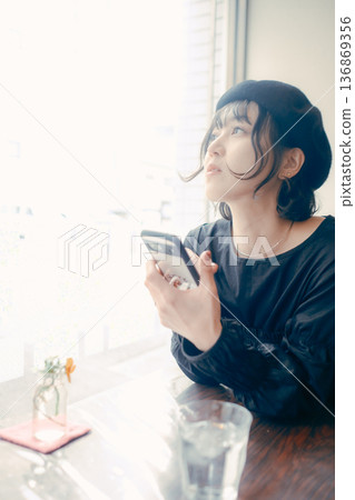 一位三十多歲的日本女性在咖啡館裡看著她的智慧型手機。 一位三十多歲的日本女性在咖啡館裡看著她的智慧型手機。 136869356