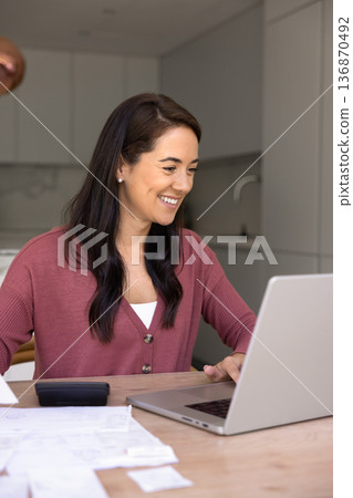 Smiling woman managing bills using laptop at home 136870492