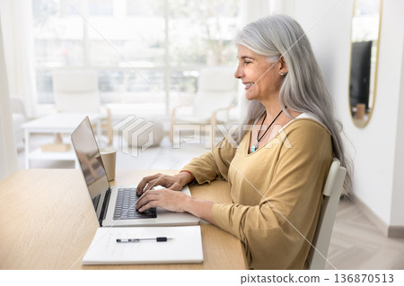 Smiling mature woman working on her laptop Smiling mature woman working on her laptop 136870513