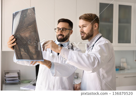 Experienced surgeon explaining x-ray image details to male doctor intern Experienced surgeon explaining x-ray image details to male doctor intern 136870520