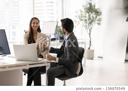 Colleagues sitting at table with laptop, shaking hands, finalizing meeting Colleagues sitting at table with laptop, shaking hands, finalizing meeting 136870549