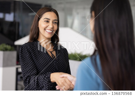 Positive Middle Eastern professional woman shaking hand with female coworker Positive Middle Eastern professional woman shaking hand with female coworker 136870568