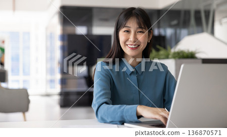 Happy young Asian businesswoman typing on laptop Happy young Asian businesswoman typing on laptop 136870571