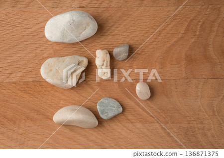 Smooth stones, of various sizes, are scattered on a wooden board Smooth stones, of various sizes, are scattered on a wooden board 136871375